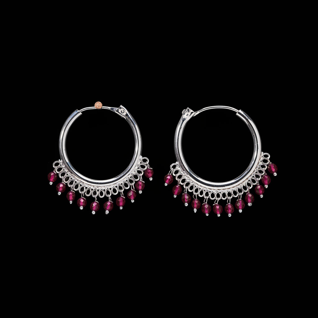 Pair of silver hoop earrings with red beads on a brown background
