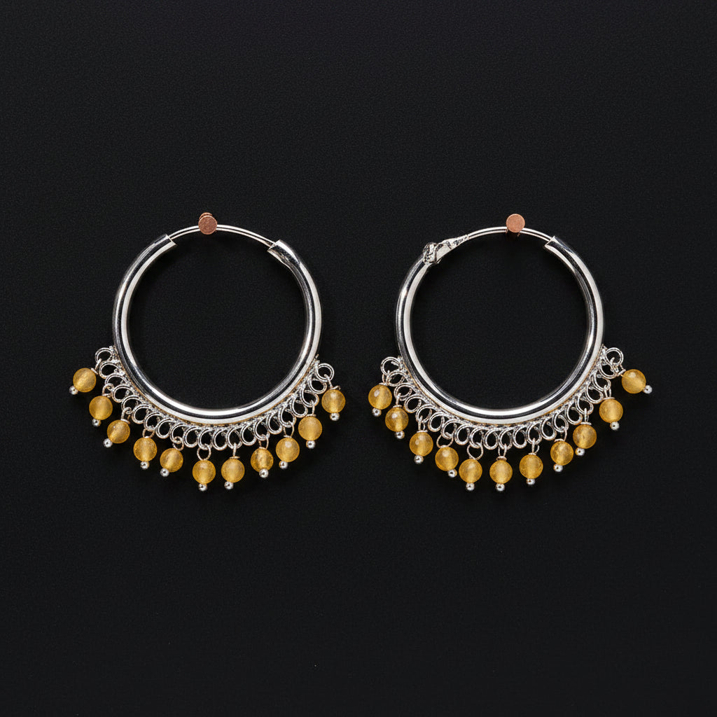 Pair of silver hoop earrings with yellow beads on a brown background