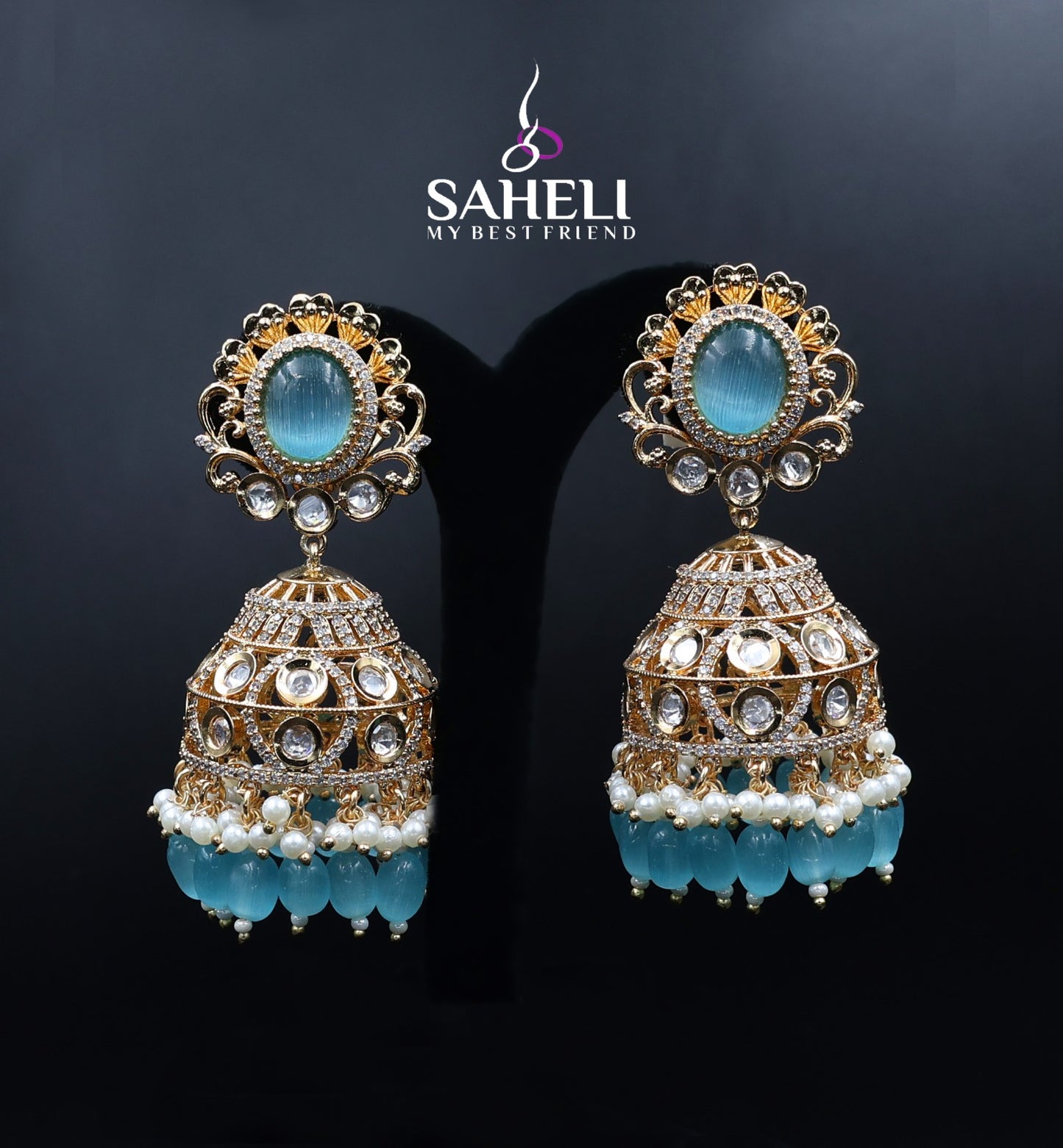 Ornate earrings with blue stones and pearl-like beads on a dark background, featuring the brand 'Saheli'.
