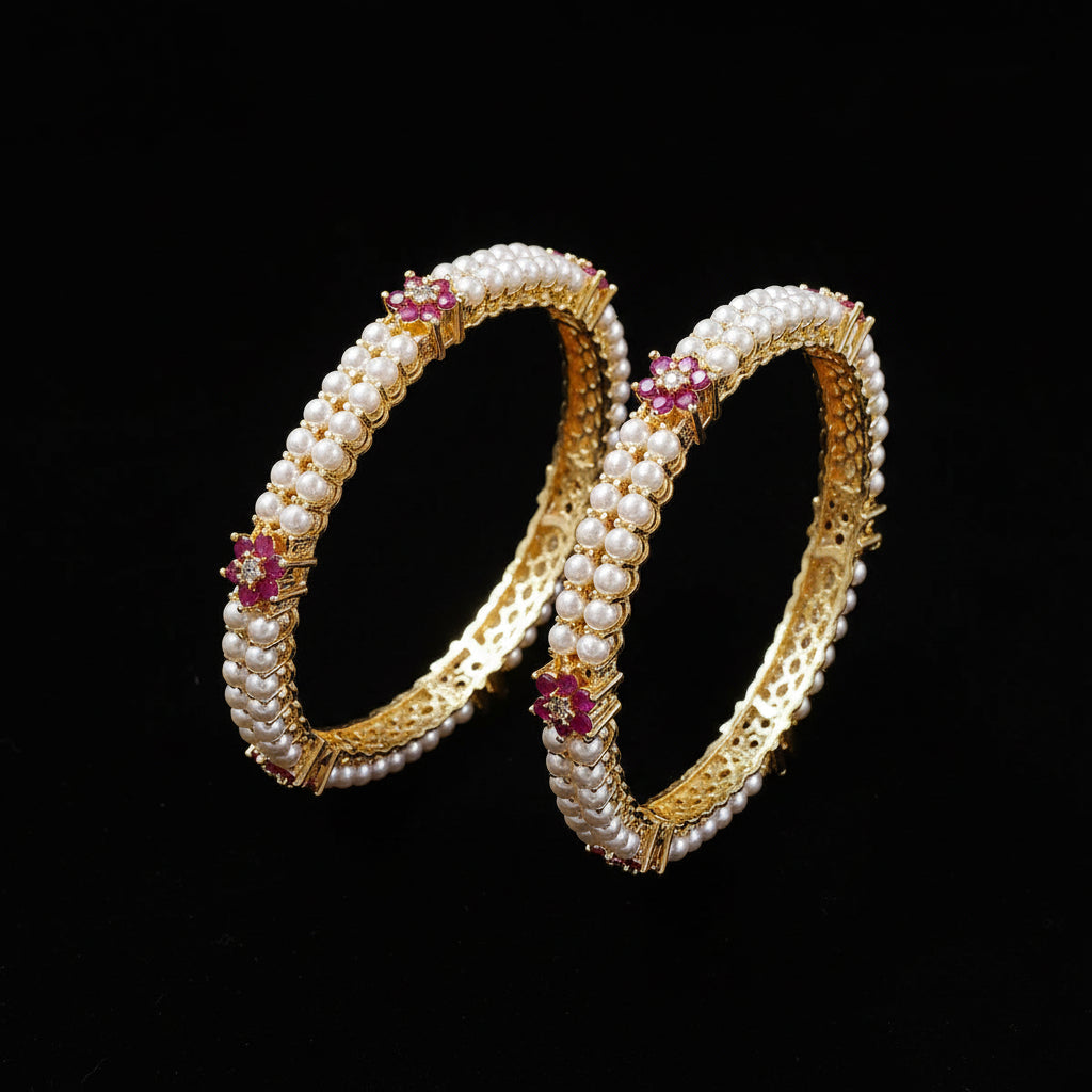 Pair of pearl bangles with gold and pink accents on a white cushion.