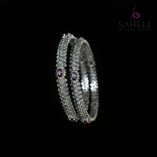 Silver bangles with purple stones on a black stand, branded 'Saheli'.