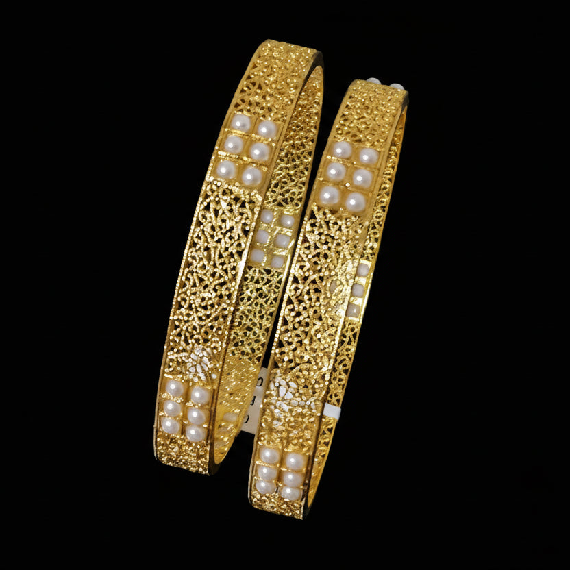 Gold bangles with pearl embellishments on a dark background, featuring the brand 'Saheli by Heera Chand'.