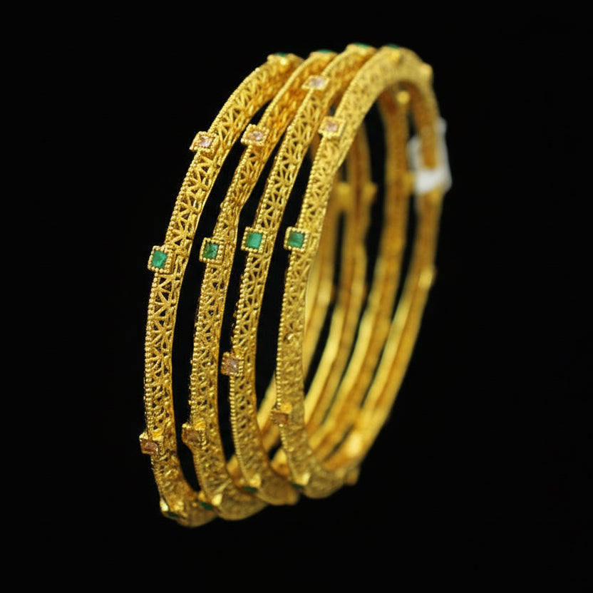 Gold bangles with green stones on a dark background, featuring the brand 'SAHELL'.