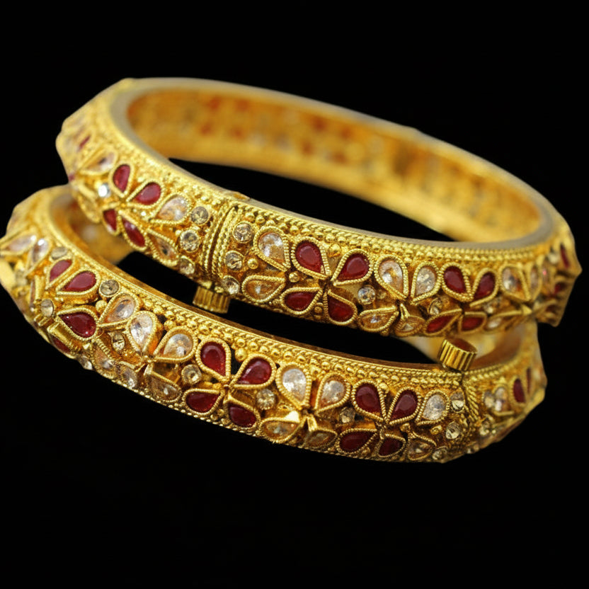 Gold bangles with red stones on a black stand, branded 'Saheli'.