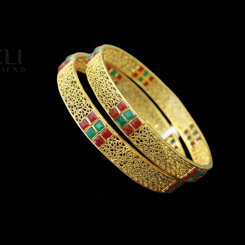 Gold bangles with embedded red and green stones on a gray background, featuring the brand 'Saheli'.