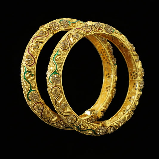 Pair of gold bangles with intricate designs on a gray background, featuring the brand 'SAHELI'.