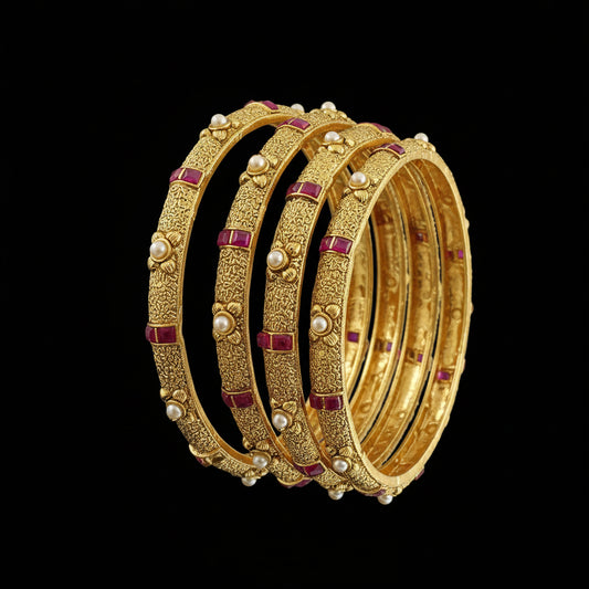 Set of gold bangles with red stones on a gray background, featuring the brand 'Saheli'.