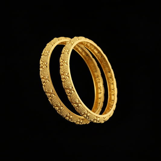 Gold bangles with intricate designs on a gray background, featuring the brand 'SAHELI'.