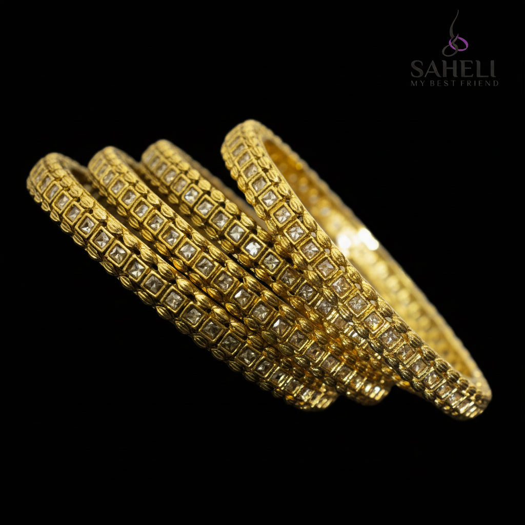 Gold bangles with embedded stones on a reflective surface, branded 'SAHELI'.
