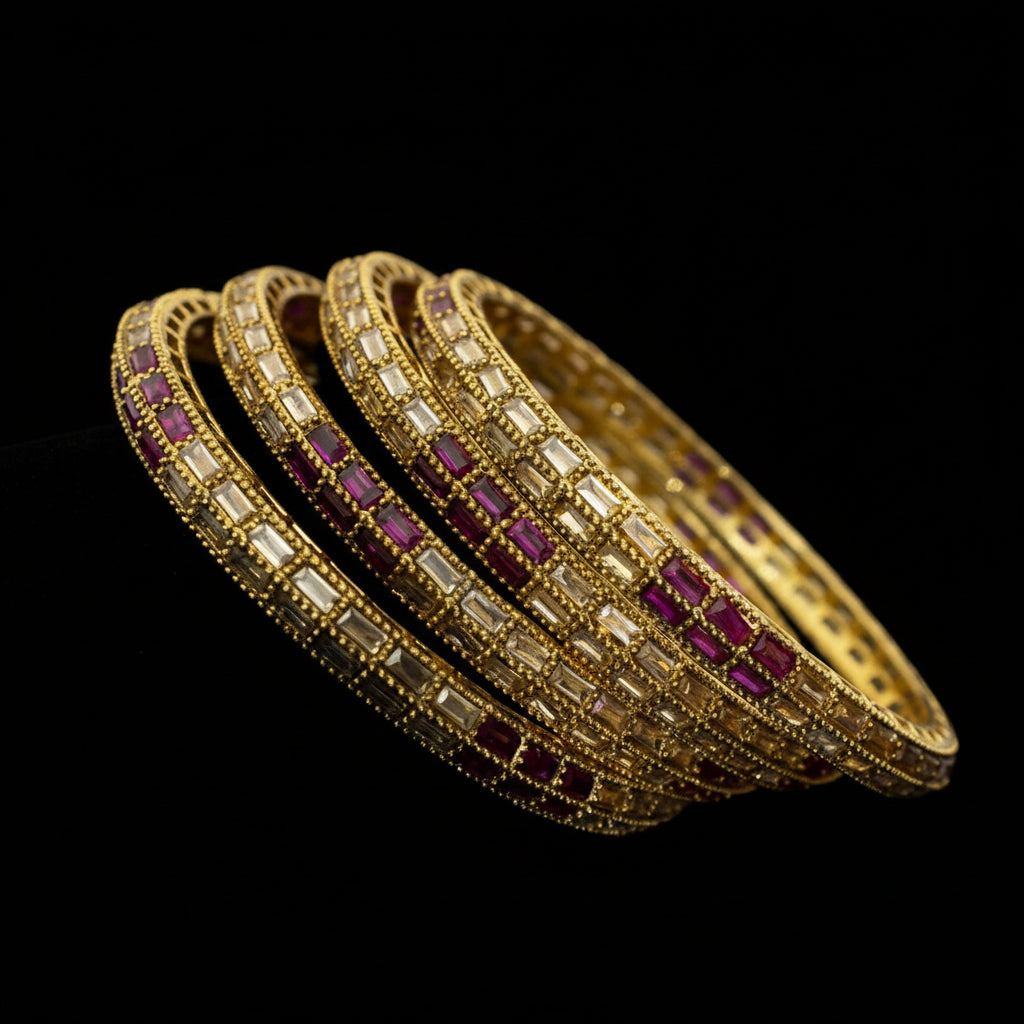 Gold bangles with red stones on a reflective surface, branded 'Saheli'.