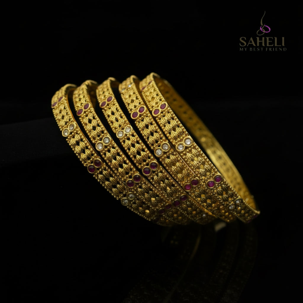 Gold bangles with red stones on a black stand, branded 'SAHELI'.