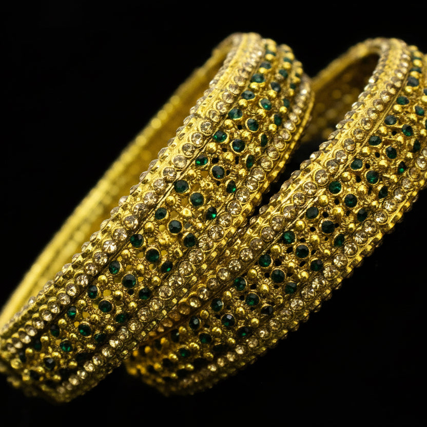 Gold bangles with green stones on a neutral background, featuring the brand 'Saheli'.