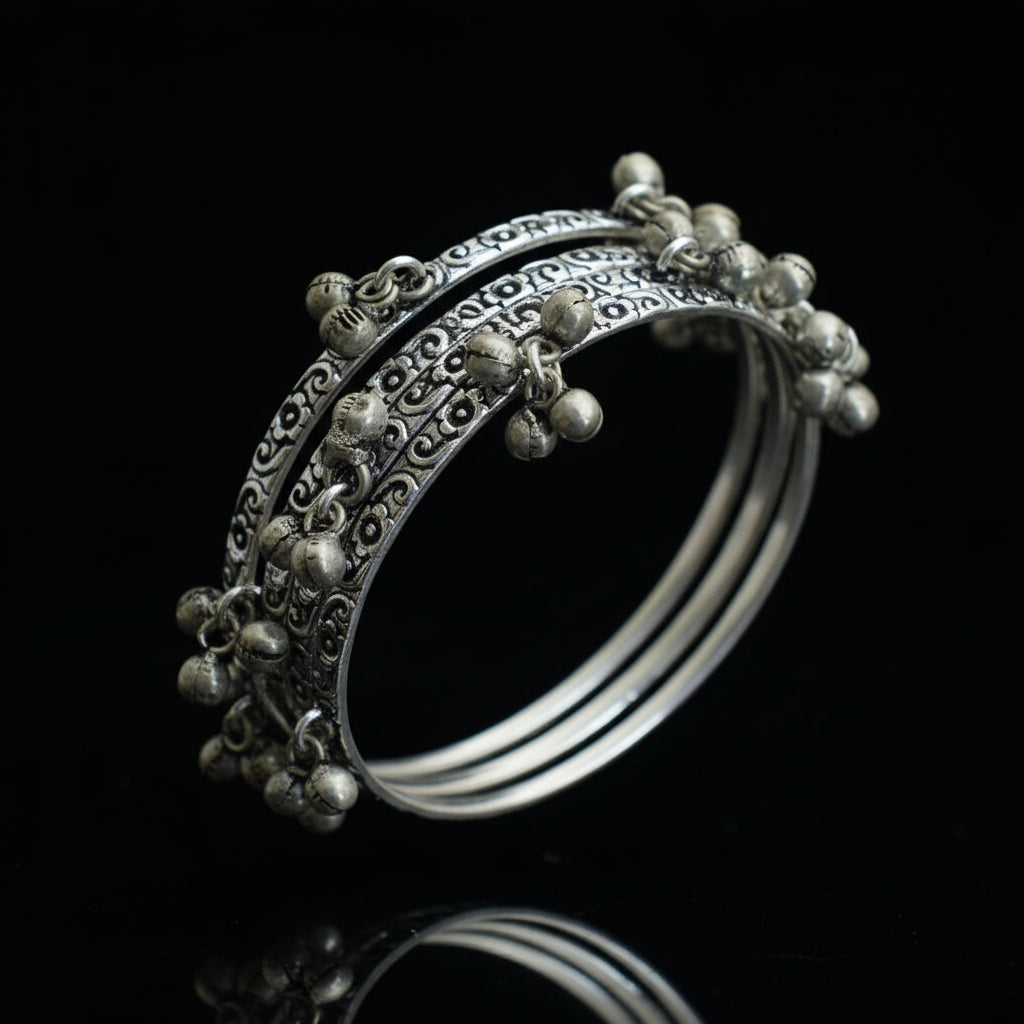 Silver bangles with intricate designs on a gray stand, branded 'Saheli'.