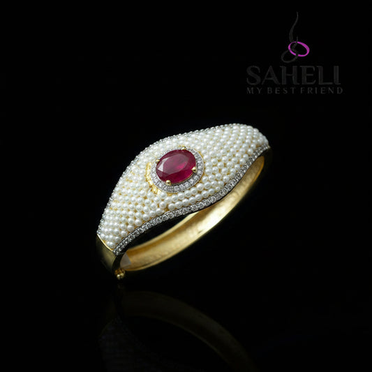 Pearl-encrusted ring with a red gemstone on a dark background, branded 'SAHELI'.