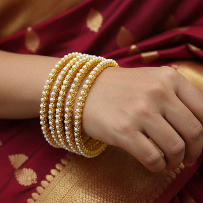 Set of gold and pearl bangles on a gray background with 'SAHELLI' branding.