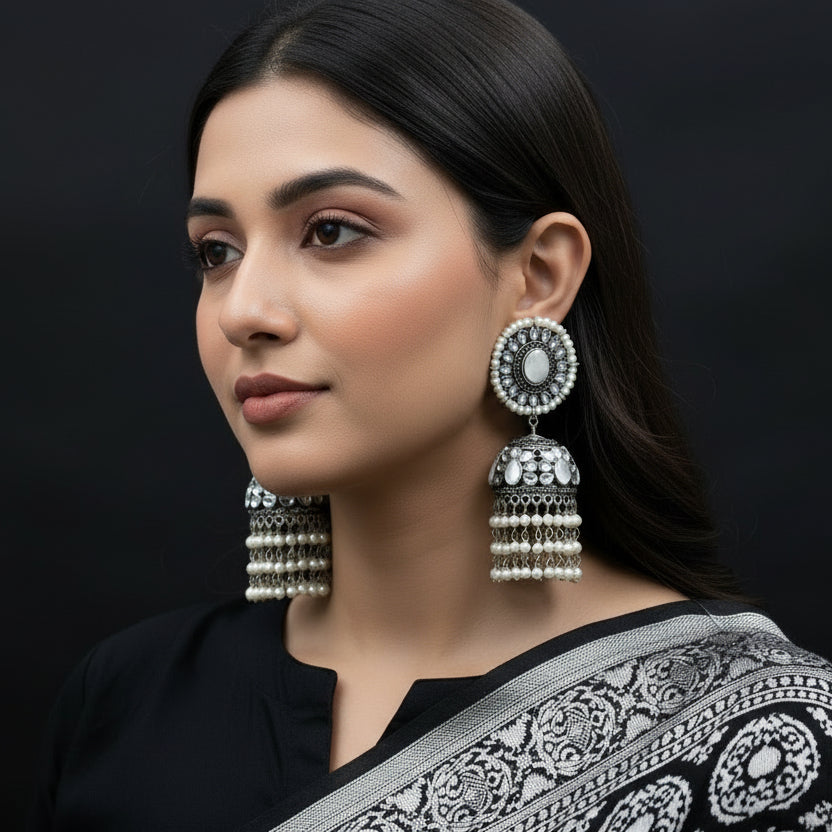 Pair of silver and pearl earrings on a stand with 'Saheli' branding.