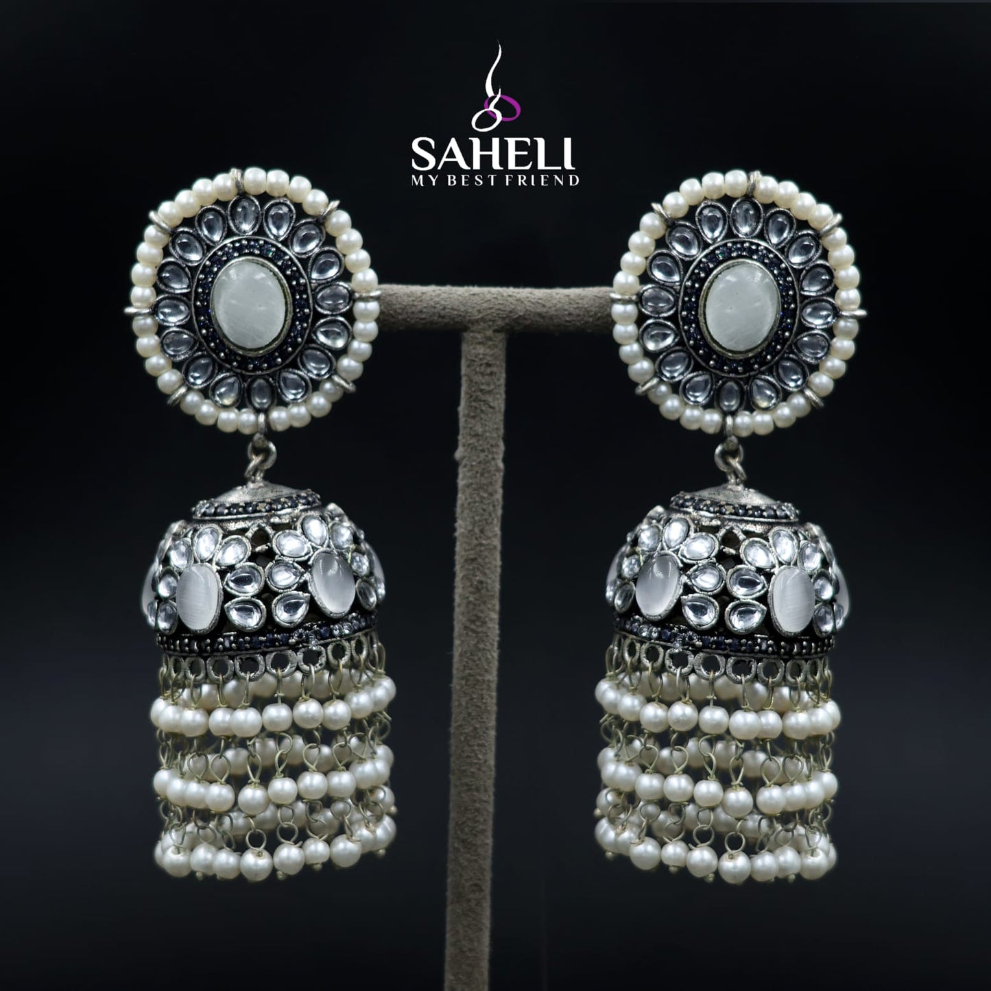 Pair of silver and pearl earrings on a stand with 'Saheli' branding.