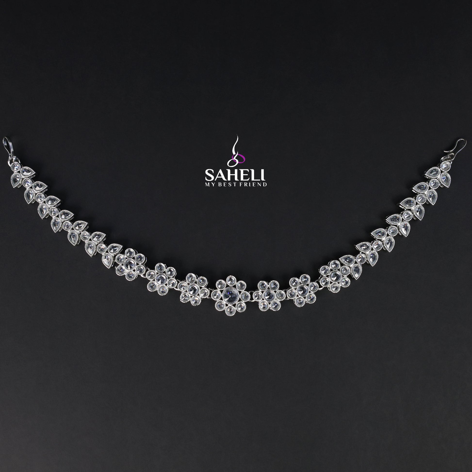 Silver necklace with floral design on a black background, featuring the brand 'Saheli'.