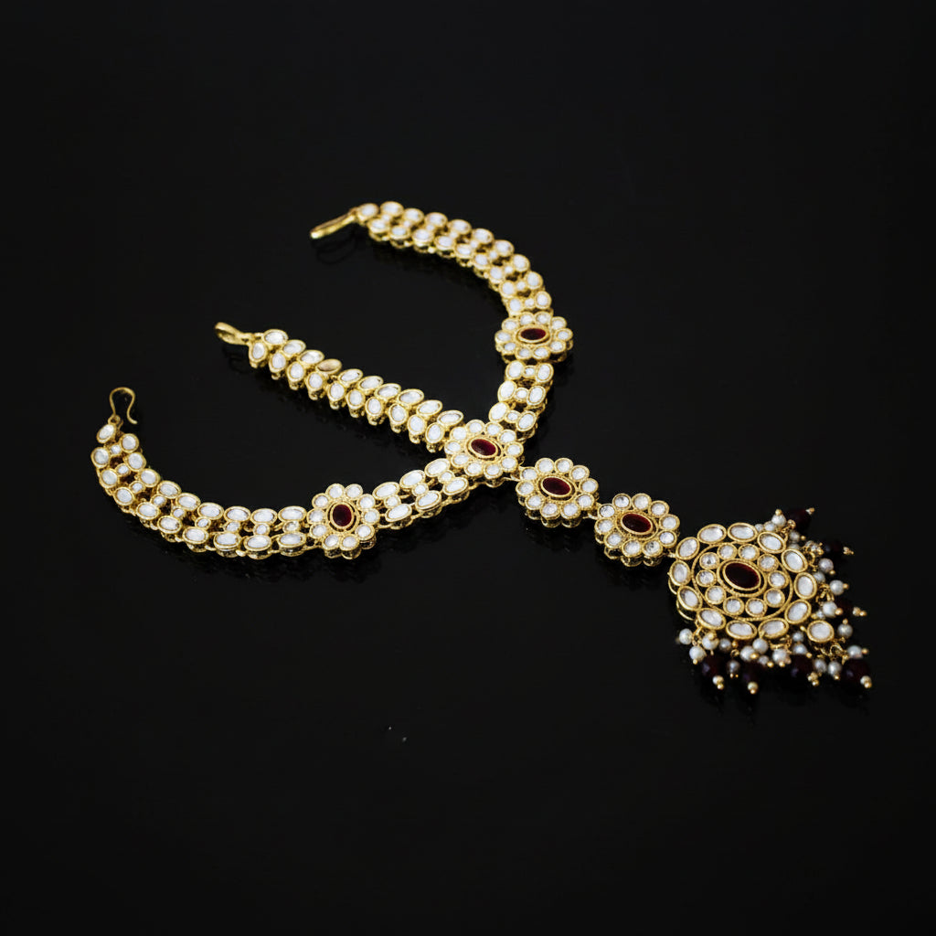 Gold necklace with red gemstones on a dark background, branded 'Saheli'.
