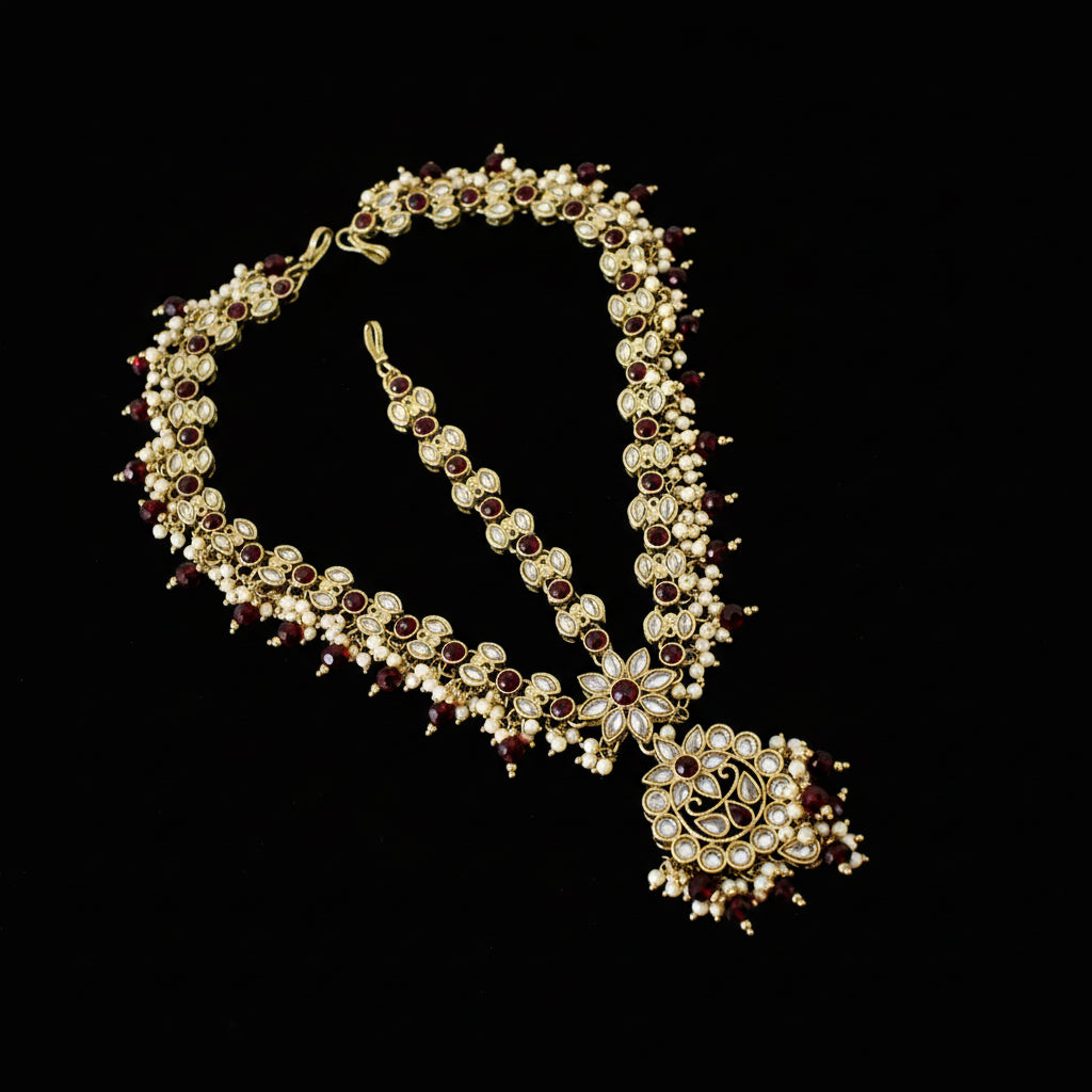 Ornate necklace with red stones on a gray background, featuring the brand 'Saheli'.