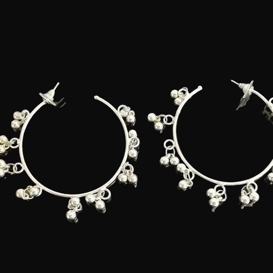 Silver hoop earrings with dangling beads on a dark background, featuring the brand 'Saheli'.