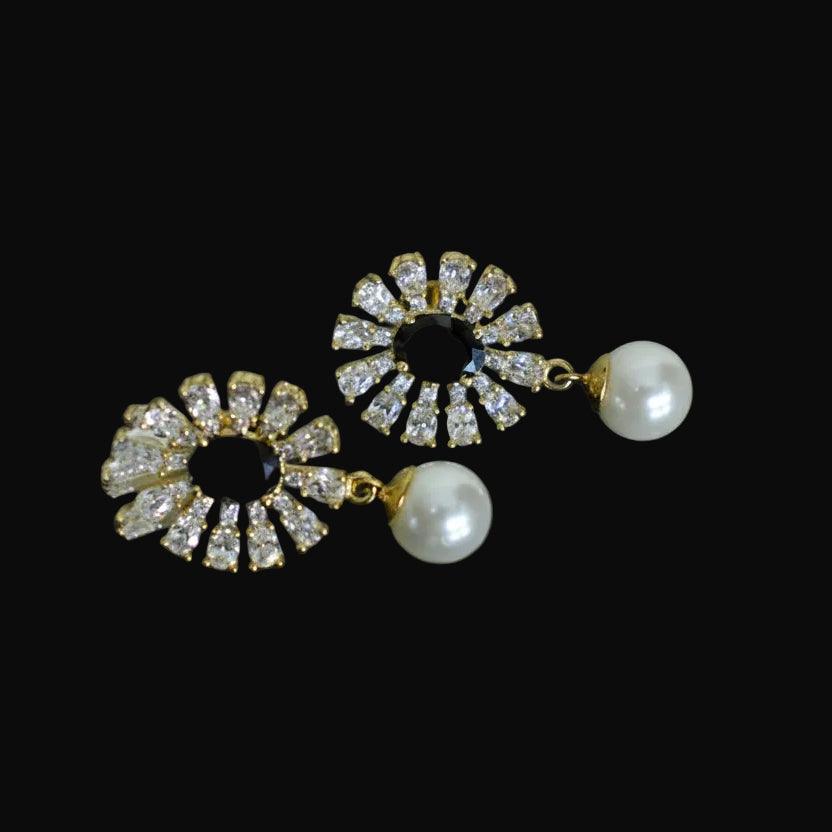 Pair of earrings with gemstones on a dark background, branded 'SAHELI'.