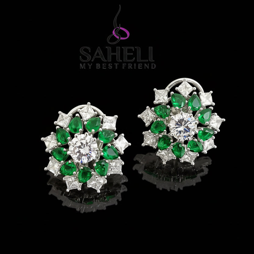 Pair of earrings with green gemstones and clear stones on a dark background, branded 'Saheli'.