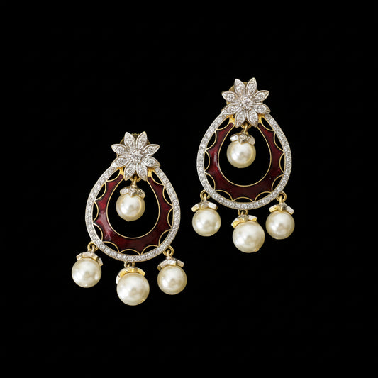 A pair of ornate gold and silver-toned statement earrings with deep red enamel inlays, white pearls, and clear rhinestone floral accents, displayed on a dark reflective surface with the Saheli My Best Friend logo in the background.