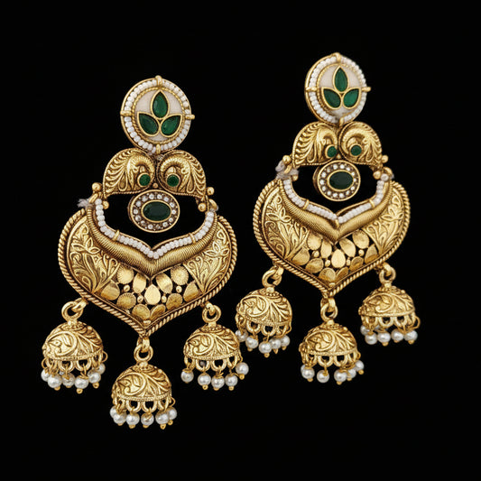 Ornate gold earrings with green and black accents on a textured black surface