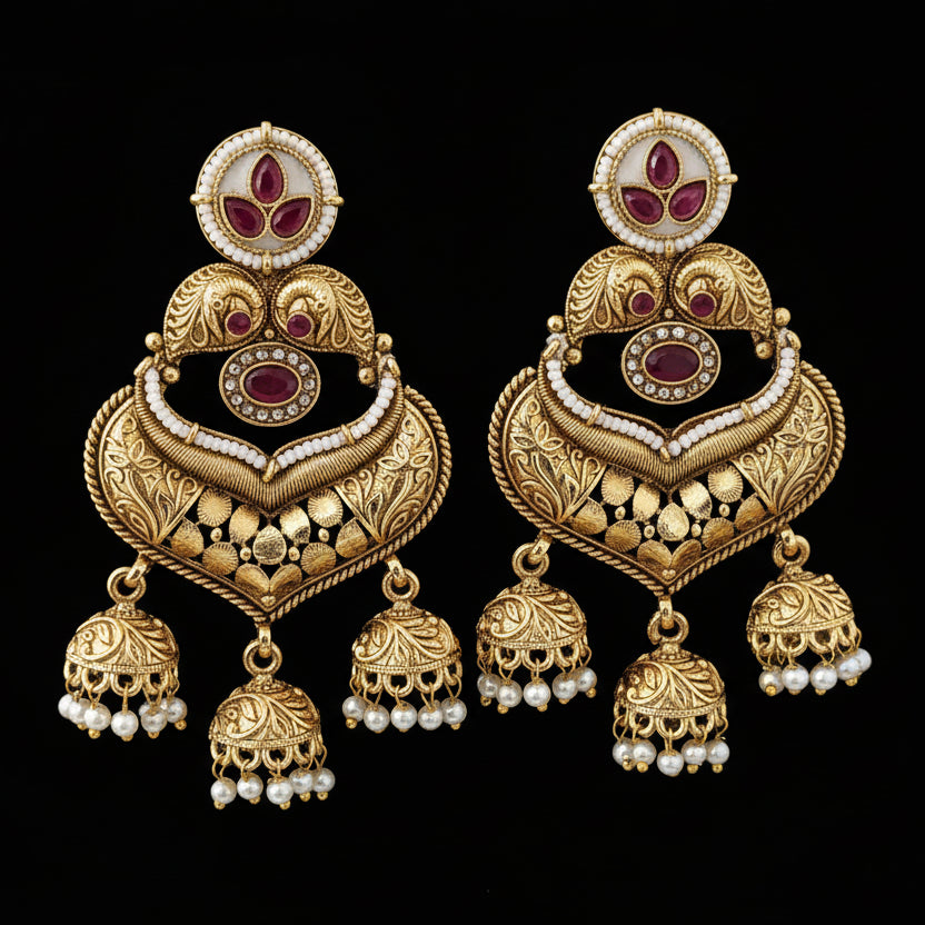 Ornate gold earrings with red stones and pearl-like beads on a textured black surface.