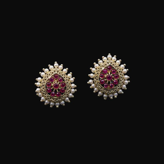 Gold and red gemstone earrings on a black stand with 'Saheli' branding.