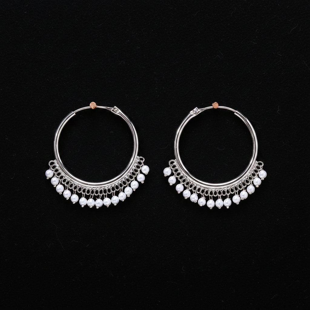 Pair of silver hoop earrings with pearl-like beads on a brown background