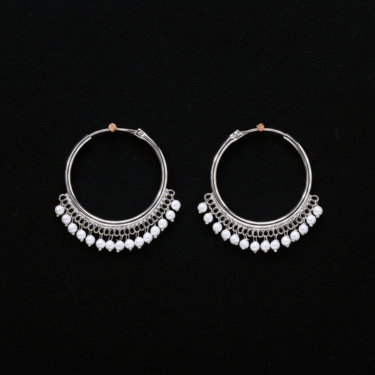 Pair of silver hoop earrings with pearl-like beads on a brown background