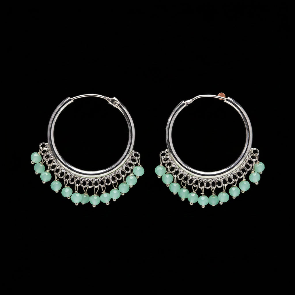 Silver hoop earrings with green beads on a brown background