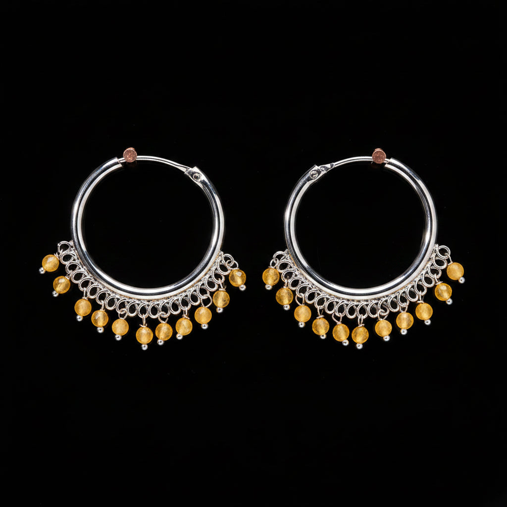 Pair of silver hoop earrings with yellow beads on a brown background