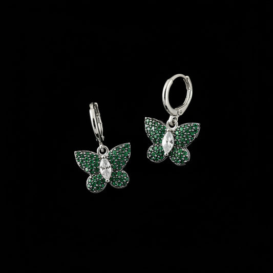 Butterfly-shaped earrings with green gemstones on a dark background, branded 'Saheli'.