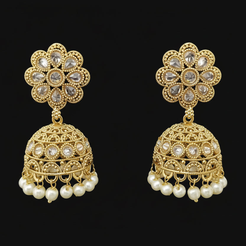 Gold earrings with floral designs and pearl accents on a gray stand against a black background