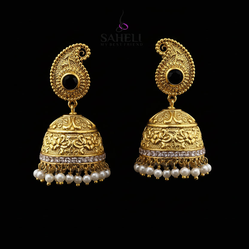 Gold jhumka earrings with pearls and black stones on a gray background, branded 'Saheli'.