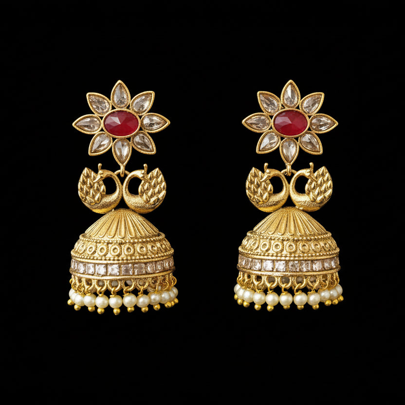Gold earrings with red gemstones on gray stands, branded 'Saheli'.