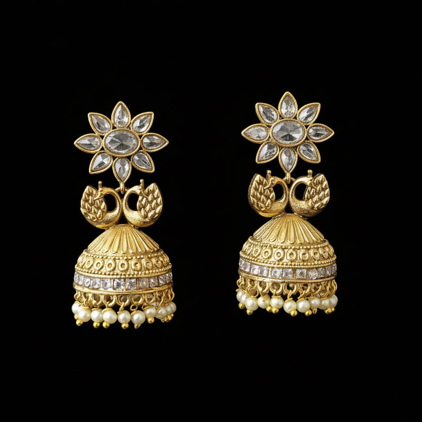 Gold jhumka earrings on a gray stand with 'Saheli' branding.