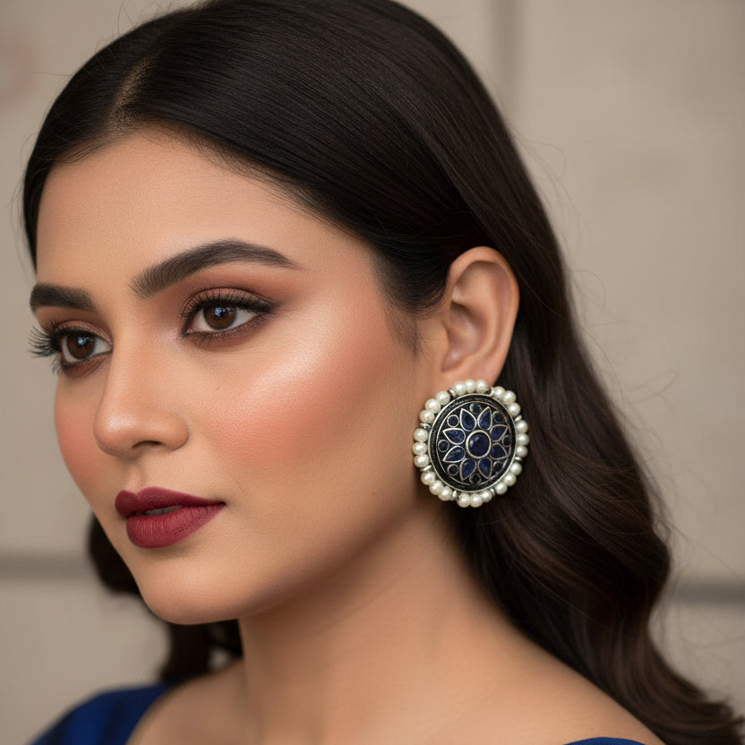 Pair of earrings with blue floral design and pearl accents on a dark background