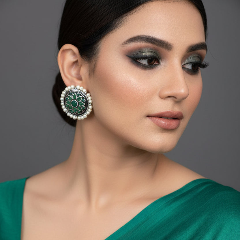 Pair of earrings with green floral design and pearl accents on a dark background