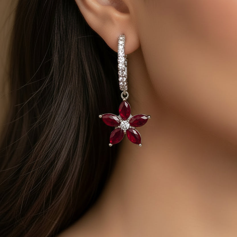 Flower-shaped earrings on a black stand with 'Saheli' branding.