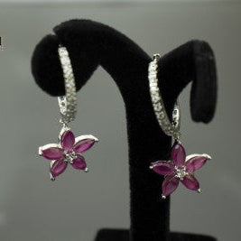 Flower-shaped earrings on a black stand with 'Saheli' branding.