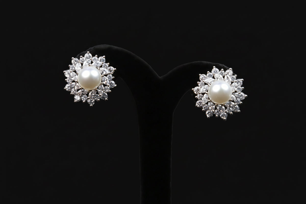 Pearl earrings with diamond accents on a black stand, branded 'Saheli'.