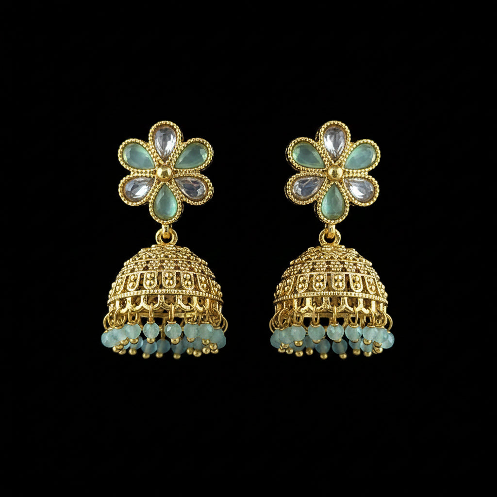 A pair of gold-plated Indian jhumka earrings with light blue stone accents and dangling bead fringes, displayed on a textured blue background.