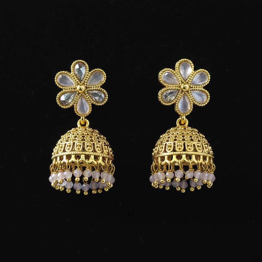 A pair of gold-plated Indian jhumka earrings with light blue stone flower studs and dangling bell-shaped charms, set against a solid blue background.