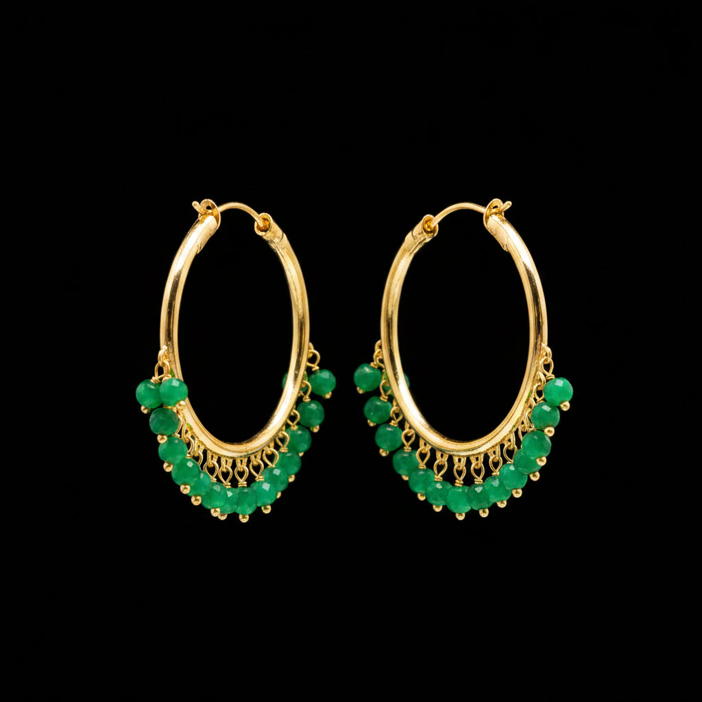 A pair of gold hoop earrings with dangling pearl-like bead clusters, photographed on a gray textured surface with a small white price tag attached to one earring.