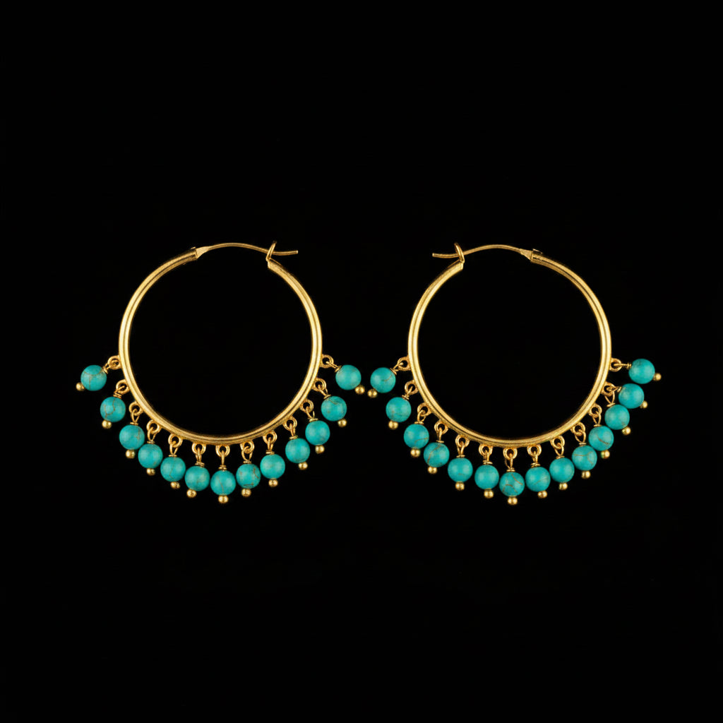 A pair of gold hoop earrings with dangling pearl-like bead clusters, photographed on a gray textured surface with a small white price tag attached to one earring.