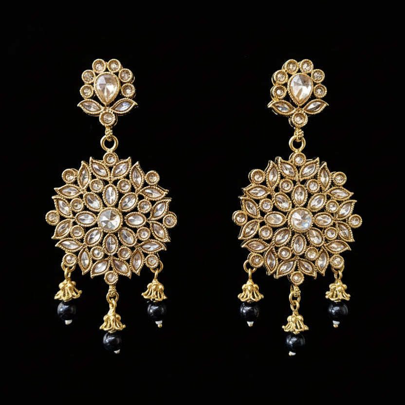 Gold and black earrings on a gray stand with 'SAHELI' branding.